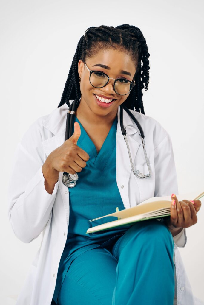 pexels photo 19131215 19131215 Confident female doctor in scrubs smiling and giving a thumbs up, representing healthcare professionalism.
